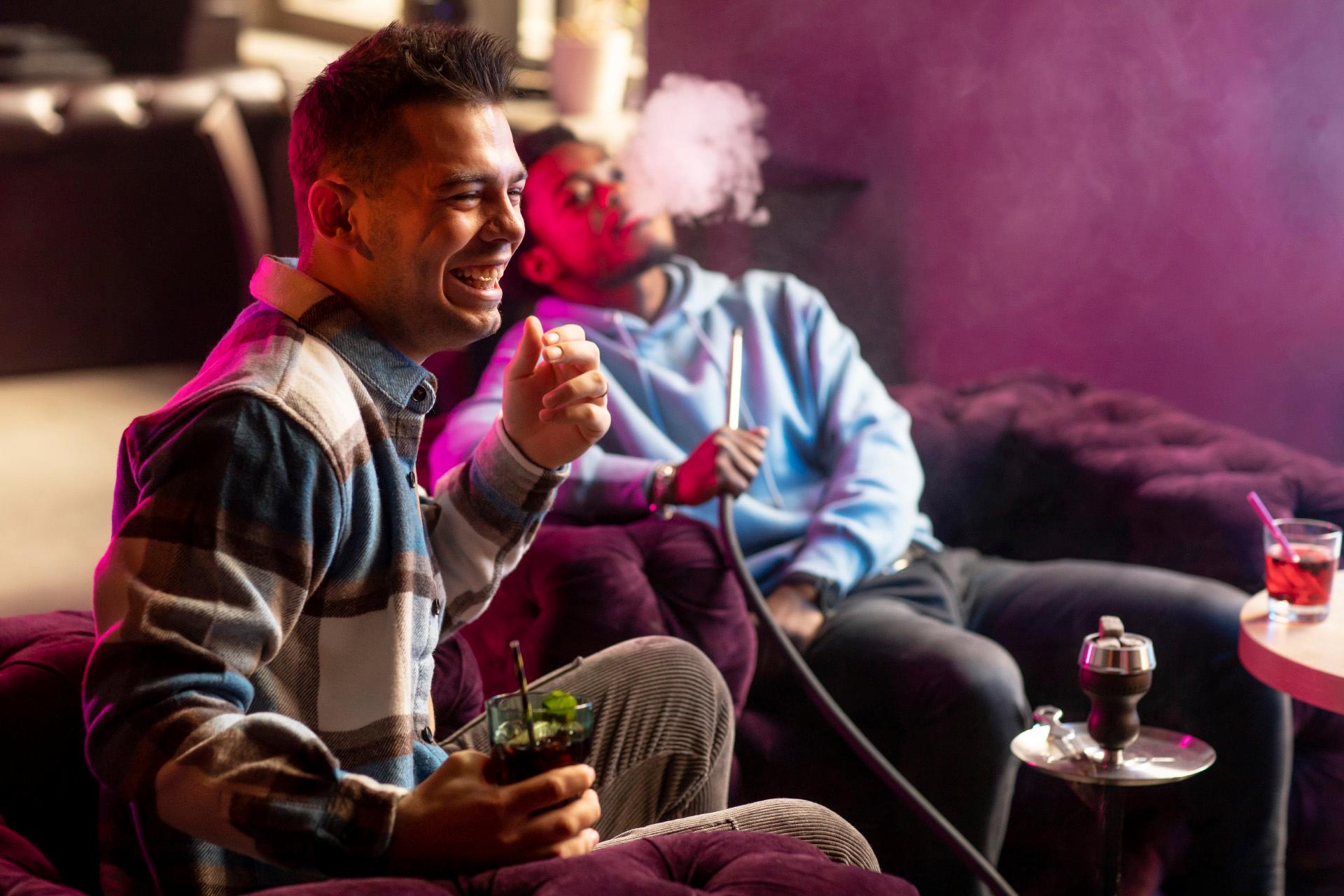 Young men vaping from hookah indoors